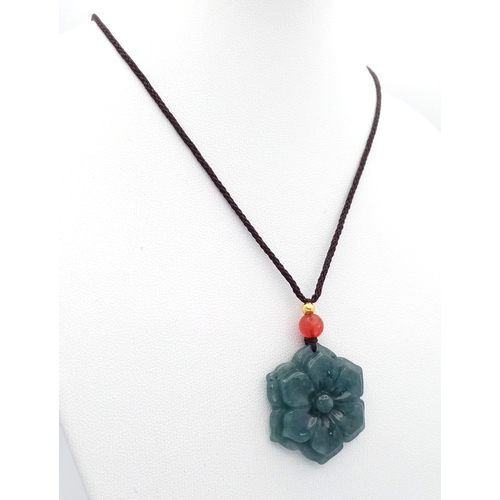 384 - A natural green jadeite blossom flower pendant on rope chain, 2.5cm diameter, 64cm rope length.