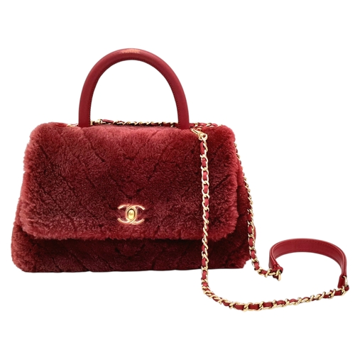 A Chanel Burgundy Shearling Coco Top Handle Bag. Burgundy textile exterior with gold tone hardware, top handle, detachable shoulder strap, protected base studs and twist-lock closure. Burgundy textile interior with one main compartment, a opened side pocket and a zipped side pocket. Some stains, a 3cm scratch and signs of wear to the exterior. Comes with a COA. Aprox 25cm length x 14cm height x 10cm depth. Please see photos or request the condition report. Ref: 17680.