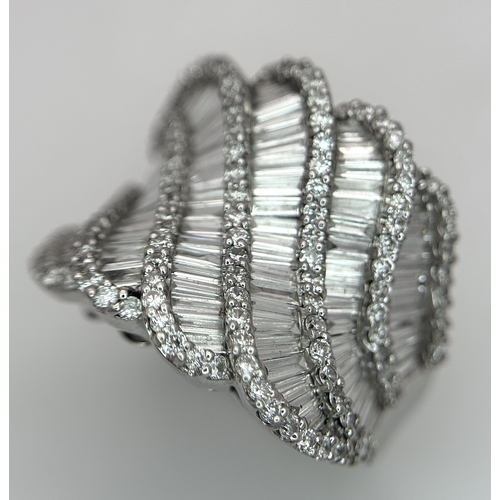134 - An 18K White Gold and Diamond Ladies Cocktail Ring. Waves of round brilliant and baguette cut diamon... 