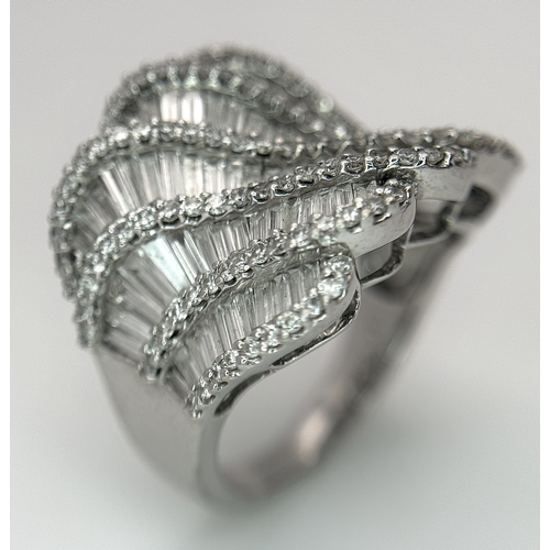 134 - An 18K White Gold and Diamond Ladies Cocktail Ring. Waves of round brilliant and baguette cut diamon... 