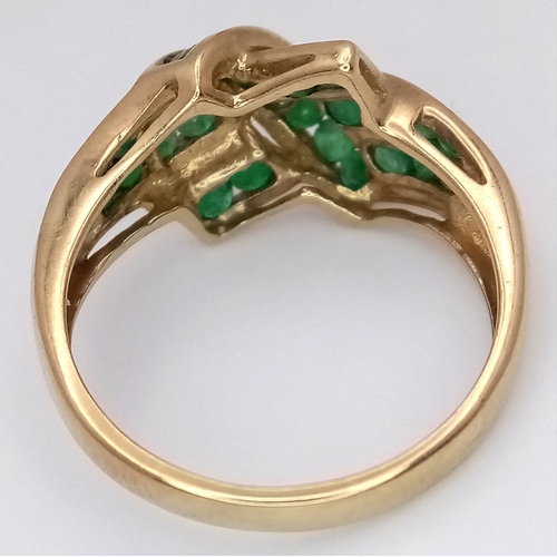 1032 - A 9K Yellow Gold Emerald Crossover Ring. Channel set stones. Size O. 3g total weight.