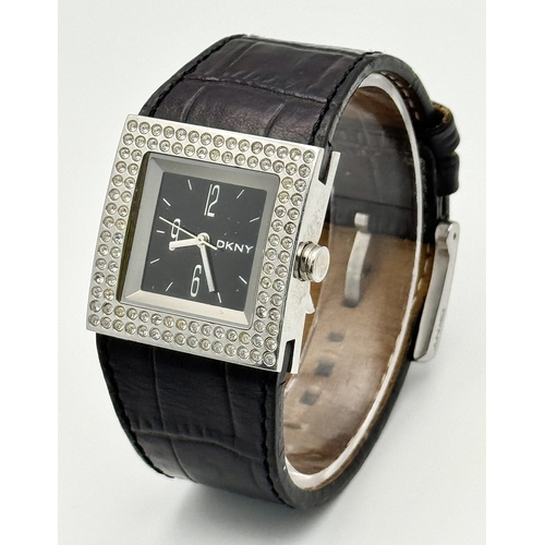 1064 - A DKNY, STONE SET, SQUARE FACE, BLACK LEATHER STRAP WATCH. WITH ORIGINAL STRAP AND BUCKLE. IN FULL W... 