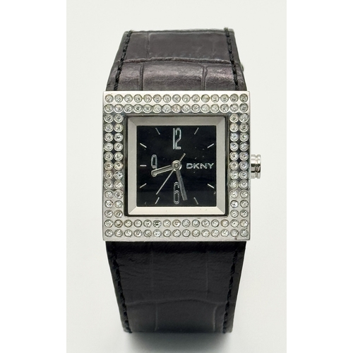 1064 - A DKNY, STONE SET, SQUARE FACE, BLACK LEATHER STRAP WATCH. WITH ORIGINAL STRAP AND BUCKLE. IN FULL W... 