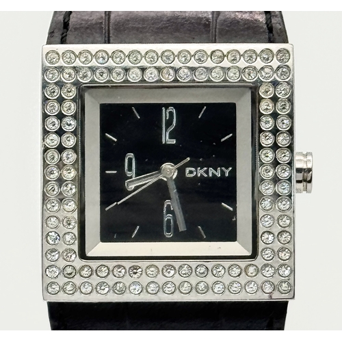 1064 - A DKNY, STONE SET, SQUARE FACE, BLACK LEATHER STRAP WATCH. WITH ORIGINAL STRAP AND BUCKLE. IN FULL W... 