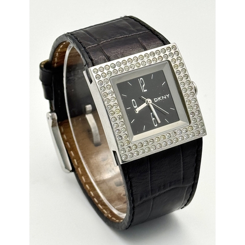 1064 - A DKNY, STONE SET, SQUARE FACE, BLACK LEATHER STRAP WATCH. WITH ORIGINAL STRAP AND BUCKLE. IN FULL W... 