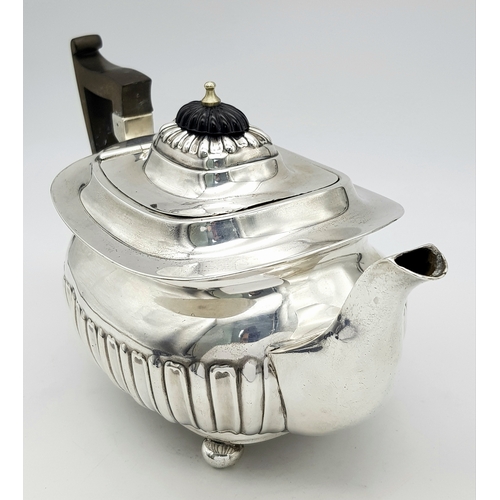 188 - An Antique Sterling Silver Teapot. Part fluted body, bun feet and an angular wooden handle. Hallmark... 