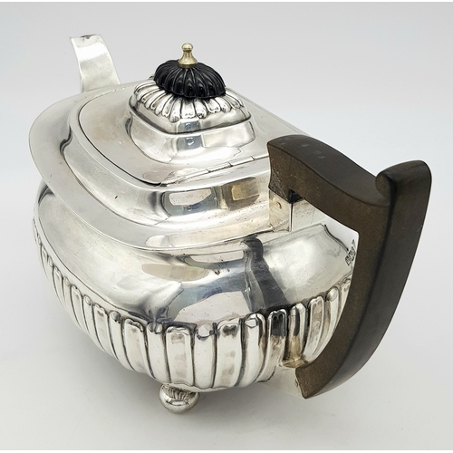 188 - An Antique Sterling Silver Teapot. Part fluted body, bun feet and an angular wooden handle. Hallmark... 
