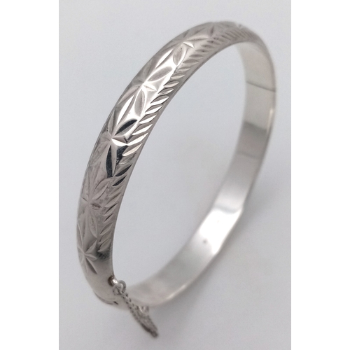 406 - A vintage hinged silver bangle. Complete with silver safety chain. Beautiful decoration to front. UK... 