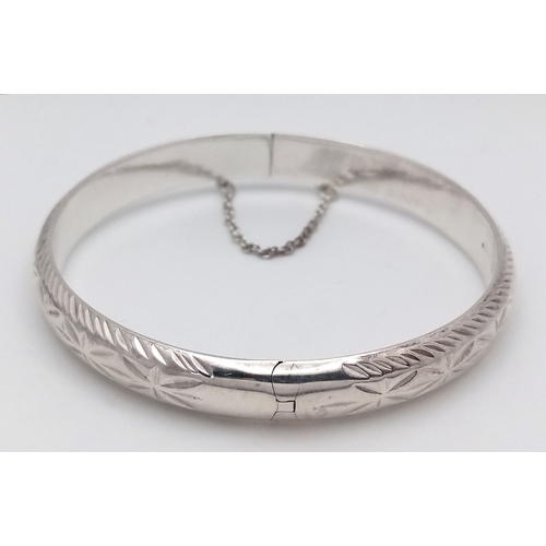 406 - A vintage hinged silver bangle. Complete with silver safety chain. Beautiful decoration to front. UK... 
