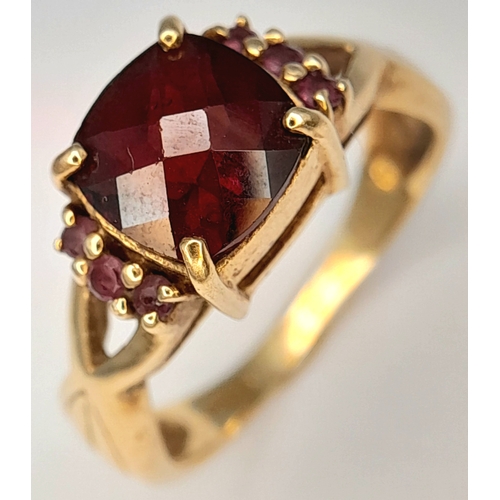 175 - A 9K Yellow Gold Garnet Ring. A cushion cut garnet c.2ct sits on a raised setting with garnet accent... 