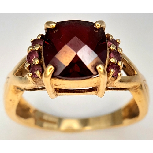 175 - A 9K Yellow Gold Garnet Ring. A cushion cut garnet c.2ct sits on a raised setting with garnet accent... 