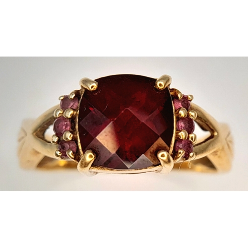 175 - A 9K Yellow Gold Garnet Ring. A cushion cut garnet c.2ct sits on a raised setting with garnet accent... 