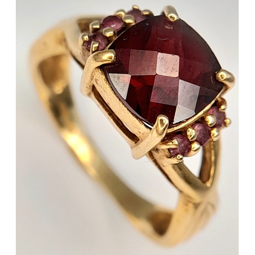 175 - A 9K Yellow Gold Garnet Ring. A cushion cut garnet c.2ct sits on a raised setting with garnet accent... 