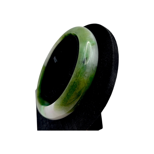 704 - A Green Jade Bangle，circular form, carved from jade of variegated green and pale tones. Inner diamet... 