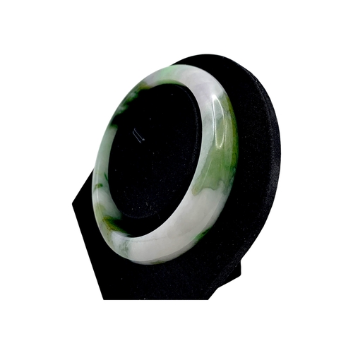 704 - A Green Jade Bangle，circular form, carved from jade of variegated green and pale tones. Inner diamet... 