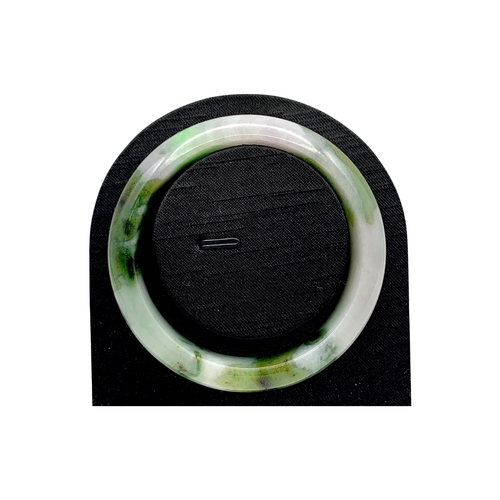704 - A Green Jade Bangle，circular form, carved from jade of variegated green and pale tones. Inner diamet... 