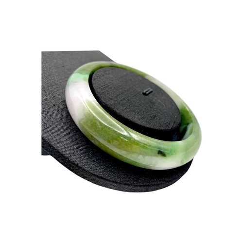 704 - A Green Jade Bangle，circular form, carved from jade of variegated green and pale tones. Inner diamet... 