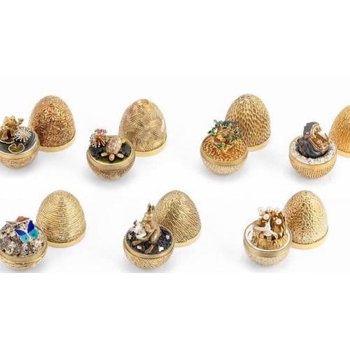 A Collection of Gilded Silver and Enamel Stuart Devlin Surprise Eggs. London 1973 - 1979, limited edition 72 of 300, with numbered booklets. London 1973 - bark effect textured surface opening to reveal a sprung patinated and silver-gilt roaring hippopotamus head issuing from a silver surround with spume decoration. London 1974 - stylised spiral bark surface opening to a model of a gilt kangaroo with a spring silver joey in the pouch, set on a patinated base with bright leaves. London 1975 - textured surface opening to reveal two sprung enamelled butterflies in orange and red, and pale and dark blue, over an open work dome of silver, silver-gilt and patinated flowers. London 1976 - chisel cut textured decoration opening to reveal a sprung patinated Robin perched within branches feeding three chicks in a nest and enamelled leaves. London 1977 - dimpled textured surface opening to reveal a sprung silver humming bird hovering among silver-gilt rushes and stems mounted with cultured pearls, all on a polished silver base. London 1978 - matted surface with stylised flower heads opening to a silver-gilt frog, leaping from a sprung green enamelled lily pad and a smaller lily pad, all on a green enamelled pond base. London 1979 - deep incised linear sectioned surface opening to reveal a silver-gilt turtle with moving head and feet, patinated rocks and red enamelled spray of flowers on a green enamelled base. All seven eggs are fully complete with original boxes and paper work. All are in very good condition.