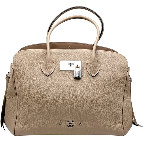 A Louis Vuitton Taupe Leather Milla MM Tote Bag. Taupe leather exterior with silver-toned hardware, dual rolled top handles, attachable shoulder strap, protected base studs, front turn-lock closure and padlock. Matching leather interior with two main compartments, a central zipped compartment and open side pockets. Approx 30cm length x 22cm height x 18cm depth. In very good condition overall. Comes with a certificate of authenticity, clochette, keys, leather tag and dust cover. Please see photos or request a condition report. Ref: 28710.