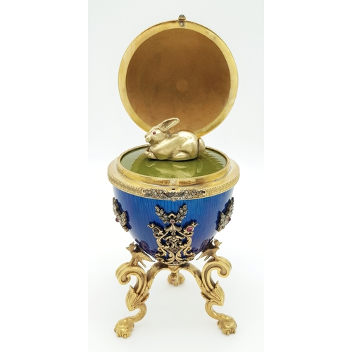 A Russian Style Diamond Set Gilded Silver and Enamel Surprise Egg. Russian Imperial style &lsquo;Easter Egg&rsquo; with ovoid silver-gilt mounted body in blue guilloche enamel, decorated with red enamel scrollwork, ribbon and laurel wreath detailing, and stone accents. Opens to reveal a rabbit figure with red stone eyes on a green enamel base. Raised on three ornate gilt feet. Comes with a presentation box. Approx 18cm height. Total weight 391.3g. UK Mainland Shipping Only or arrange a courier service.