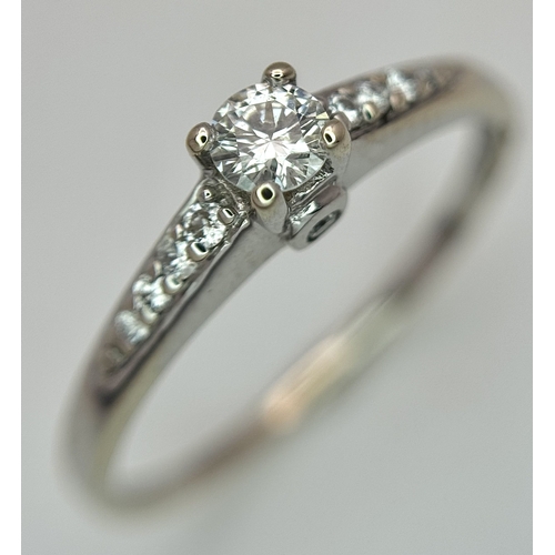 65 - An 18K White Gold, Diamond Dress Ring. 0.15ct round brilliant cut centre stone with diamond accents.... 