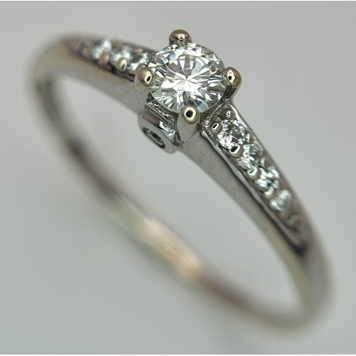 65 - An 18K White Gold, Diamond Dress Ring. 0.15ct round brilliant cut centre stone with diamond accents.... 