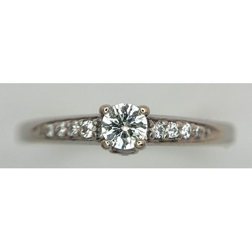 65 - An 18K White Gold, Diamond Dress Ring. 0.15ct round brilliant cut centre stone with diamond accents.... 