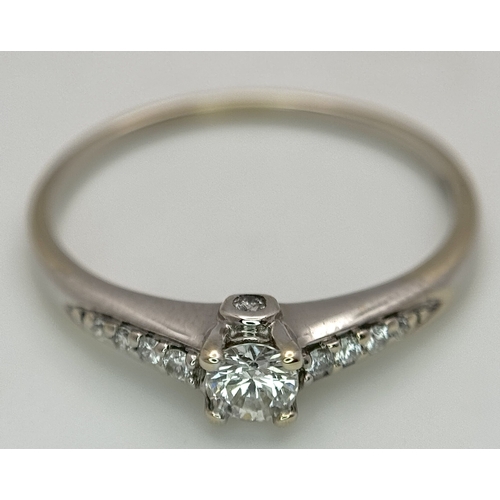 65 - An 18K White Gold, Diamond Dress Ring. 0.15ct round brilliant cut centre stone with diamond accents.... 