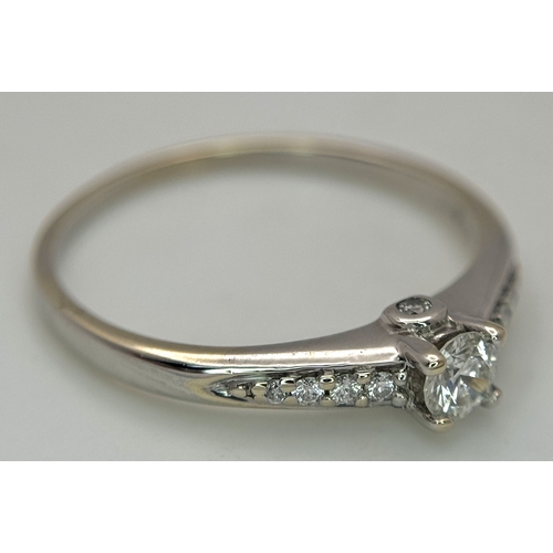 65 - An 18K White Gold, Diamond Dress Ring. 0.15ct round brilliant cut centre stone with diamond accents.... 