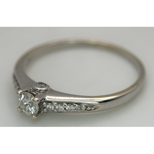 65 - An 18K White Gold, Diamond Dress Ring. 0.15ct round brilliant cut centre stone with diamond accents.... 