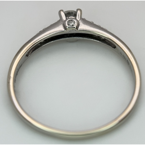 65 - An 18K White Gold, Diamond Dress Ring. 0.15ct round brilliant cut centre stone with diamond accents.... 