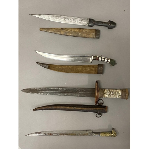 653 - A COLLECTION OF FOUR EASTERN KNIVES AND SCABBARDS. A steel bladed knife with a 25cm tapering pointed... 