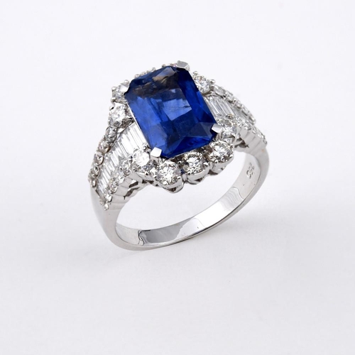 1189 - A SAPPHIRE AND DIAMOND CLUSTER RING. the rectangular-shaped sapphire is set within a surround of rou... 