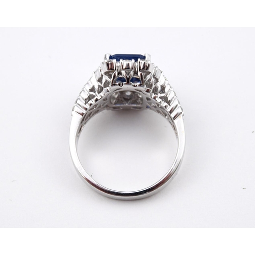 1189 - A SAPPHIRE AND DIAMOND CLUSTER RING. the rectangular-shaped sapphire is set within a surround of rou... 