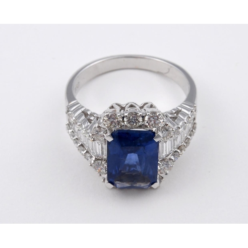 1189 - A SAPPHIRE AND DIAMOND CLUSTER RING. the rectangular-shaped sapphire is set within a surround of rou... 