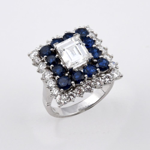 1195 - A SAPPHIRE AND DIAMOND CLUSTER RING. the rectangular step-cut diamond is set within a surround of ci... 