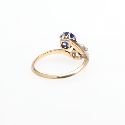 1053 - A SAPPHIRE AND DIAMOND TWO STONE CROSS-OVER RING. mounted with a circular-cut sapphire and a circula... 