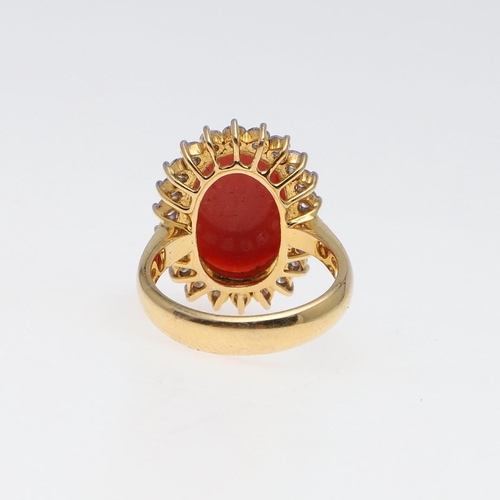 1070 - A CORAL AND DIAMOND CLUSTER RING. the oval-shaped cabochon coral is set within a surround of circula... 