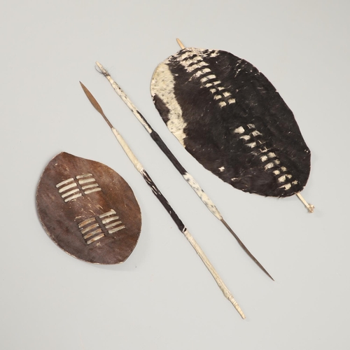 152 - TWO ZULU TYPE COWHIDE SHIELDS AND SIMILAR SPEARS. A Zulu black and whit cowhide shield 66 x 43cm wit... 