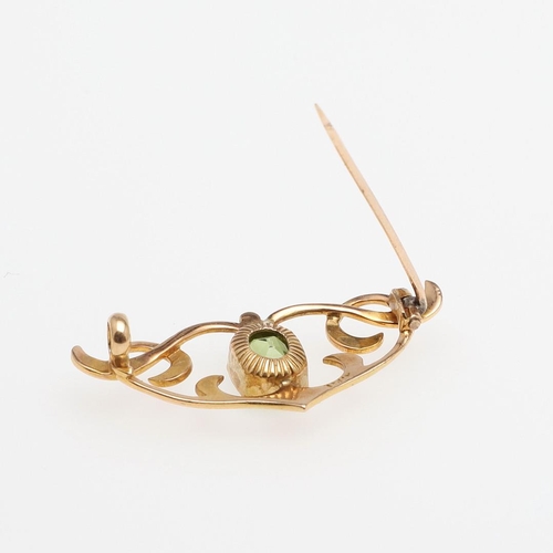 1034 - AN ART NOUVEAU PERIDOT AND 15CT GOLD BROOCH. the scrolling openwork mount is set with a rounded rect... 