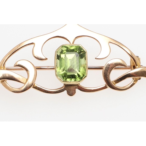 1034 - AN ART NOUVEAU PERIDOT AND 15CT GOLD BROOCH. the scrolling openwork mount is set with a rounded rect... 