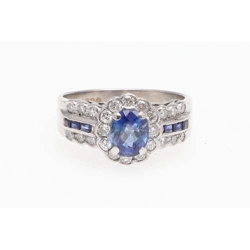 1128 - A SAPPHIRE AND DIAMOND CLUSTER RING. the oval-shaped sapphire is set within a surround of circular-c... 