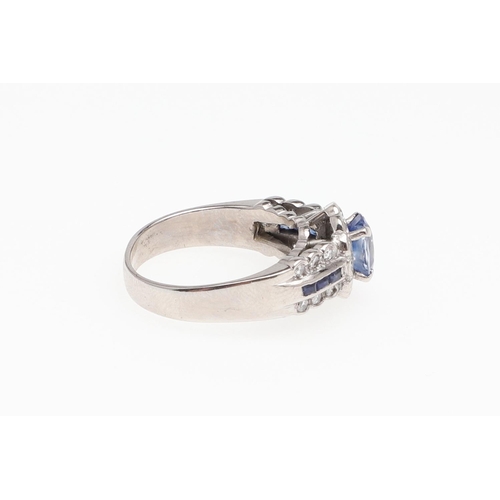 1128 - A SAPPHIRE AND DIAMOND CLUSTER RING. the oval-shaped sapphire is set within a surround of circular-c... 