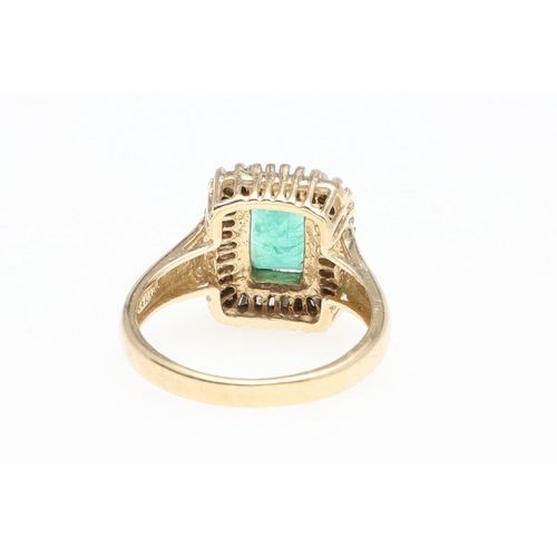 1130 - AN EMERALD AND DIAMOND CLUSTER RING. the rectangular-shaped emerald is set within a surround of tape... 