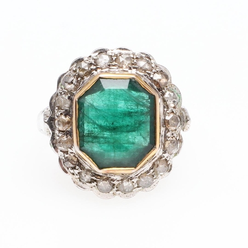 1132 - AN EMERALD AND DIAMOND CLUSTER RING. the octagonal-shaped emerald is set within a surround of circul... 