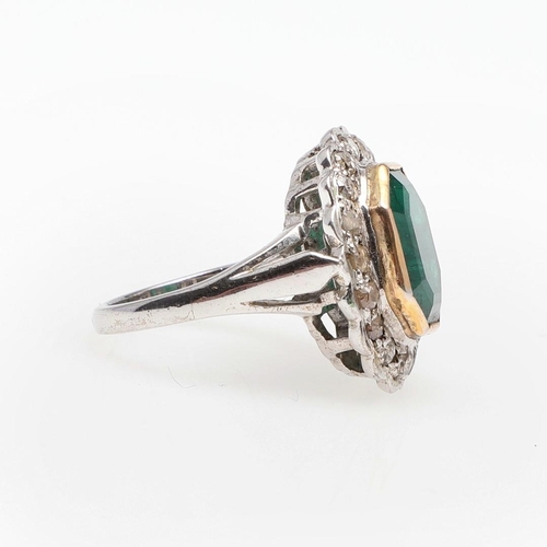 1132 - AN EMERALD AND DIAMOND CLUSTER RING. the octagonal-shaped emerald is set within a surround of circul... 