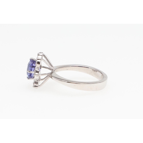 989 - A TANZANITE AND DIAMOND CLUSTER RING. the oval-shaped tanzanite is set within a surround of circular... 