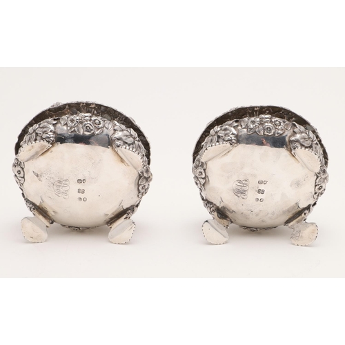 120 - A PAIR OF WILLIAM IV SQUAT CIRCULAR EMBOSSED SALTS. profusely decorated with foliage in relief and r... 