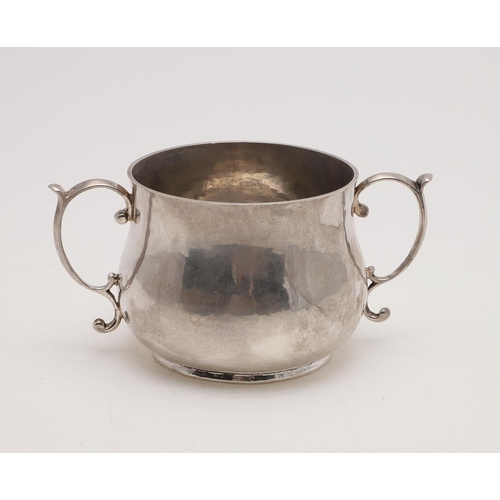 126 - AN EARLY 20TH CENTURY PORRINGER. with twin scroll handles and the bellied body with a hammered finis... 