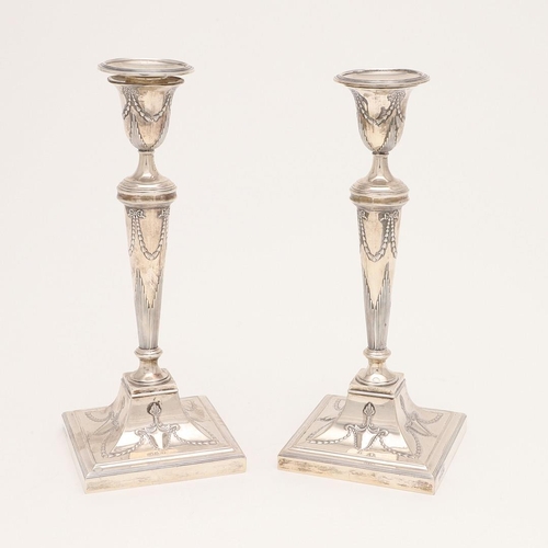 223 - A PAIR OF EDWARDIAN CANDLESTICKS. on square bases (loaded), with swag decoration, reeded borders & d... 